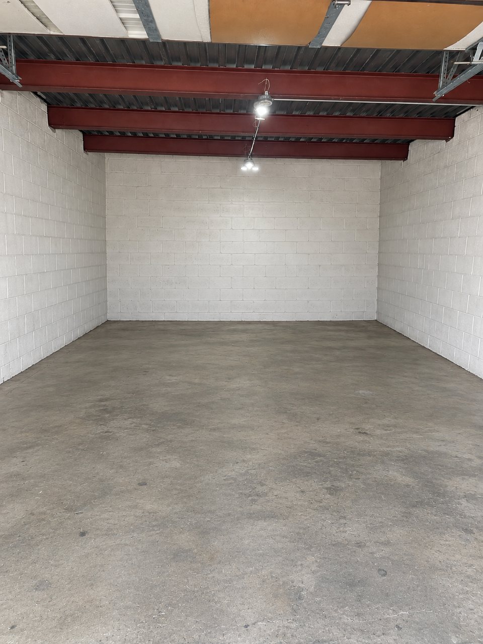 Inside a tall unit at Safe Haven Storage: painted block walls, exposed red steel beams overhead and an overhead light